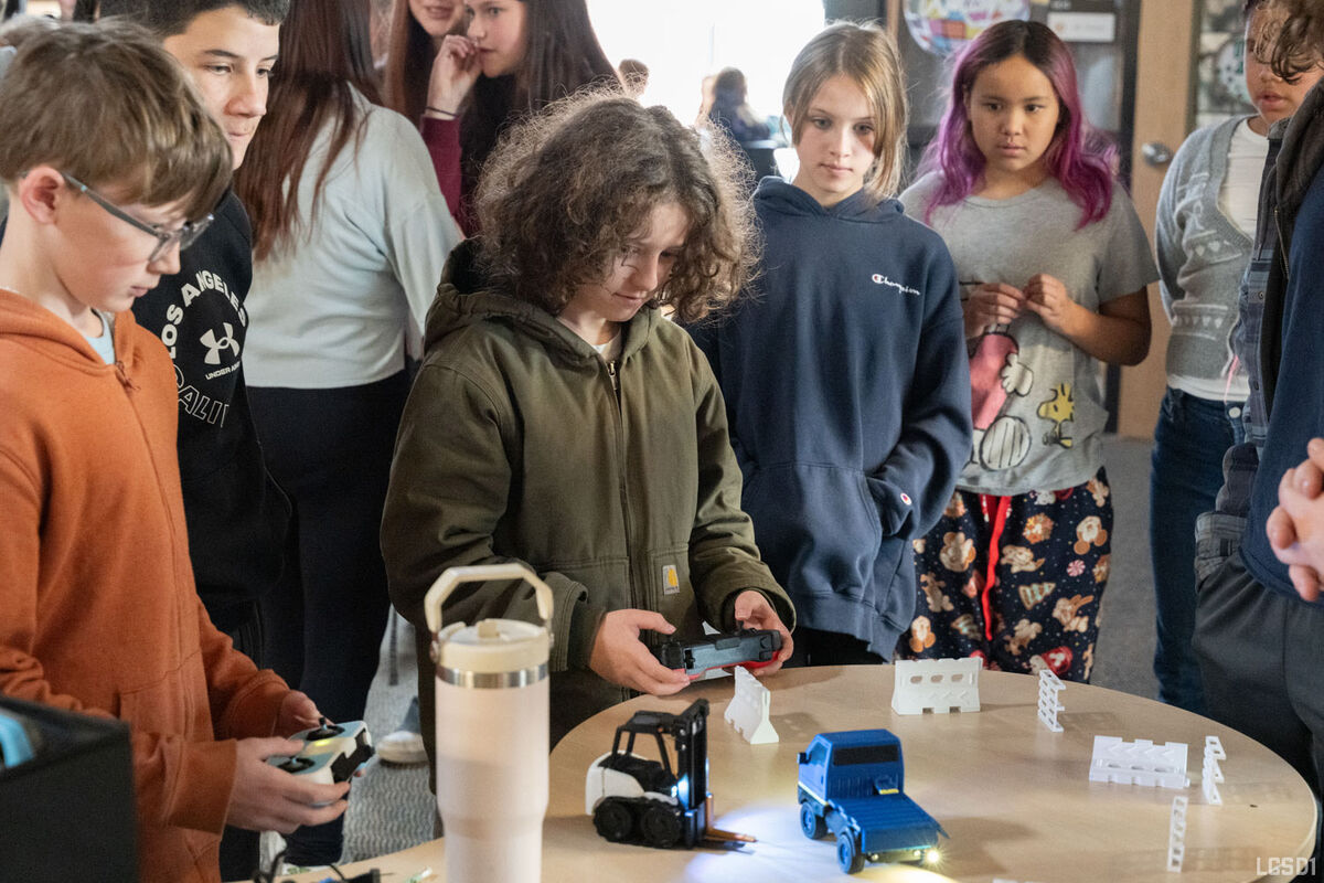 Children gather around a table, operating remote-controlled toy vehicles and building blocks.