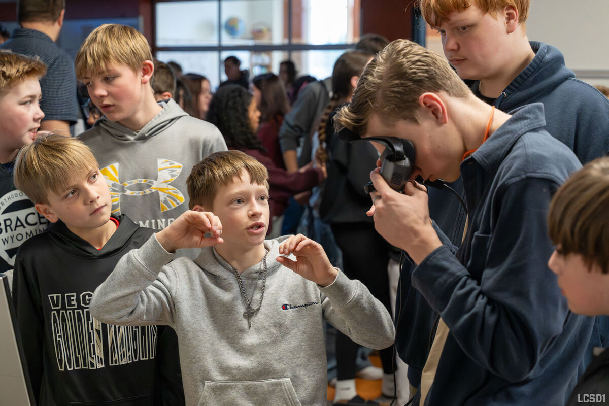 A group of young students gather around, with one looking through a device.