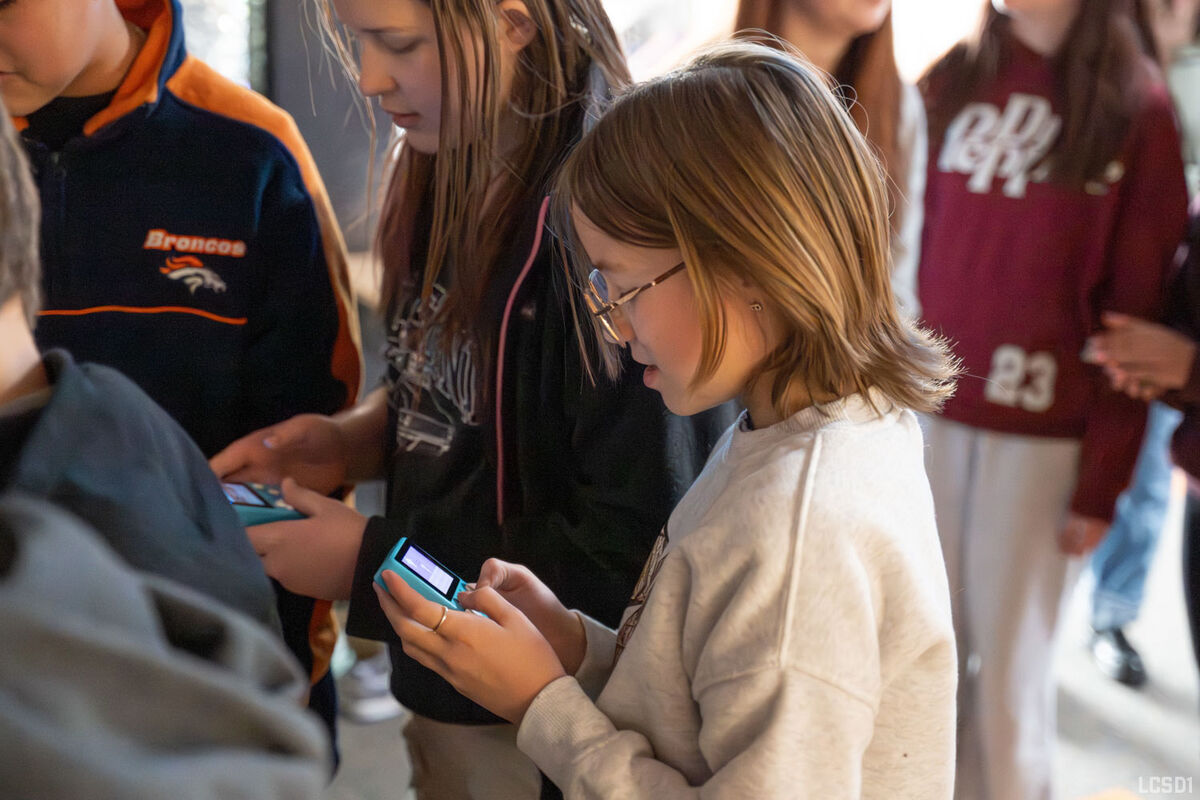 A group of children focus intently on handheld electronic devices.