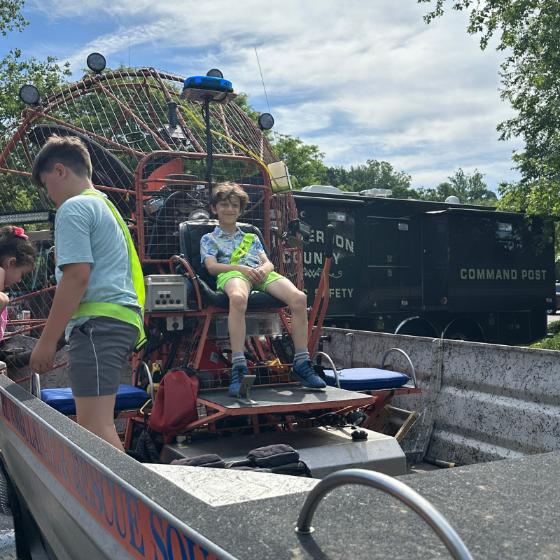 A young boy smiles while sitting in an airboat, wearing a bright green sash.