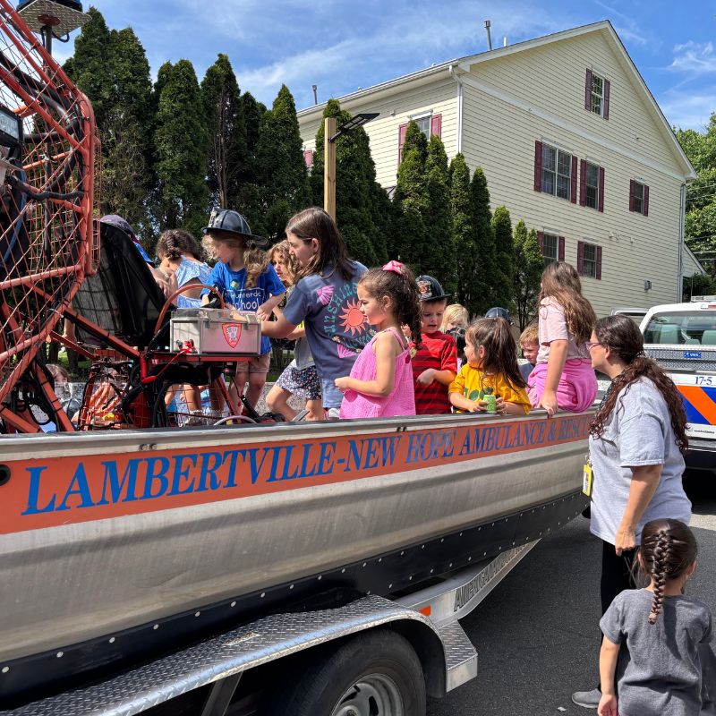 Children gather around an airboat labeled 'LAMBERTVILLE-NEW HOPE AMBULANCE & RESCUE' on a sunny day.
