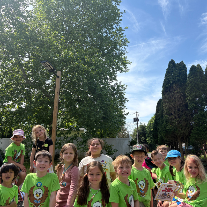 A group of smiling children in matching green shirts pose for a photo outdoors.