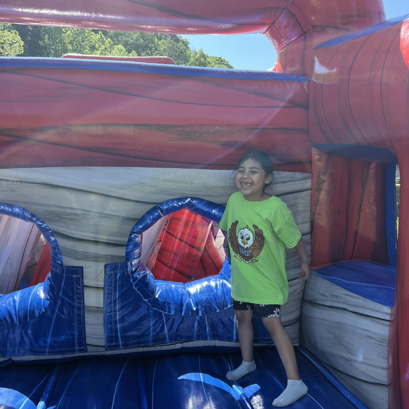 A young girl with a bright smile stands inside a colorful inflatable bounce house.