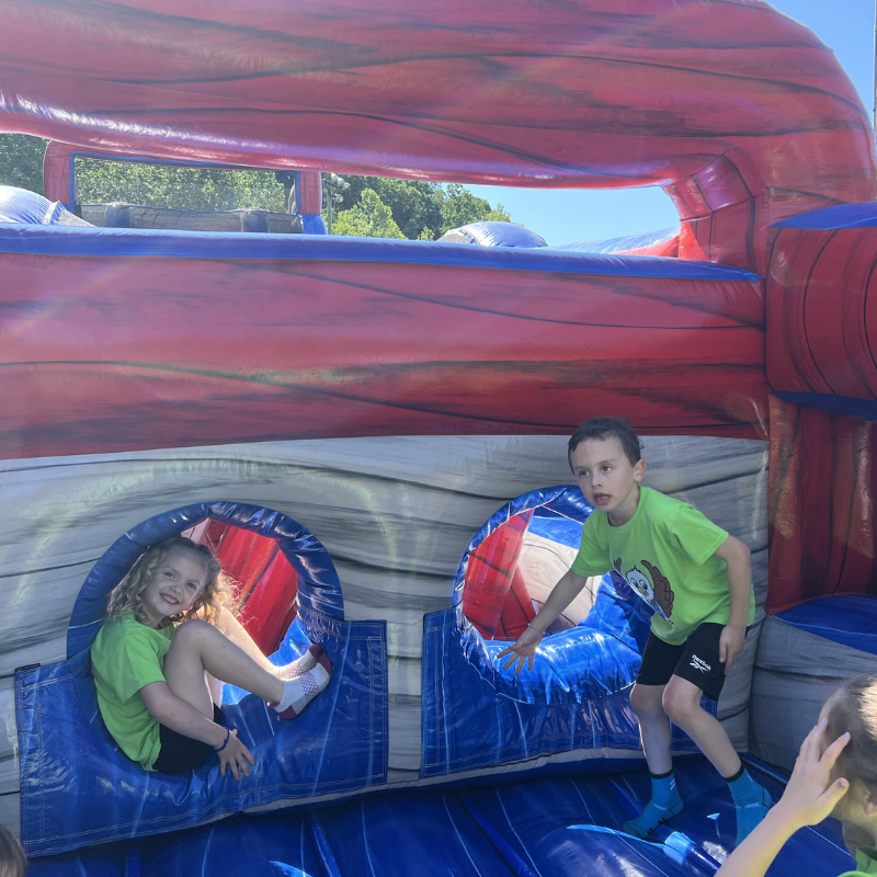 Children play inside a colorful inflatable bounce house on a sunny day.