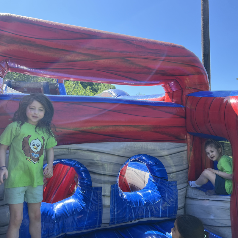 Two children play inside a large, inflatable obstacle course with red and blue sections.