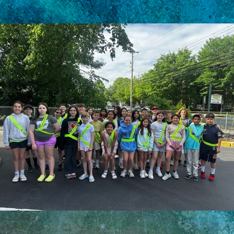A diverse group of children in bright safety vests stand together outdoors.