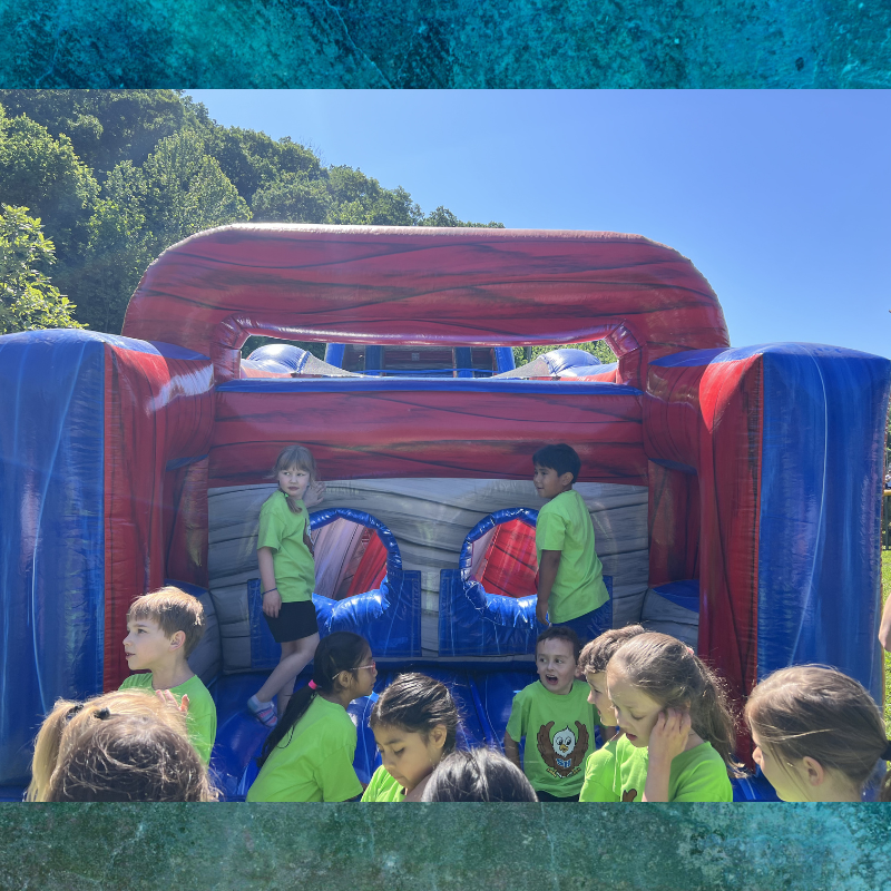 Children in bright green shirts gather around a large inflatable bounce house on a sunny day.