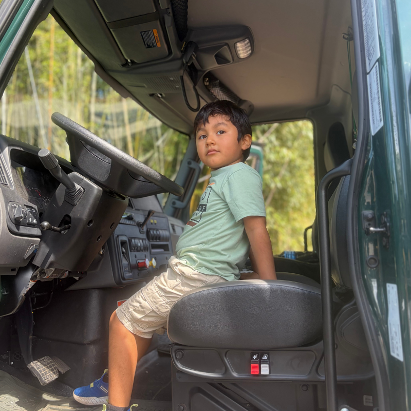 A young boy sits in the driver's seat of a large green truck, looking towards the camera.