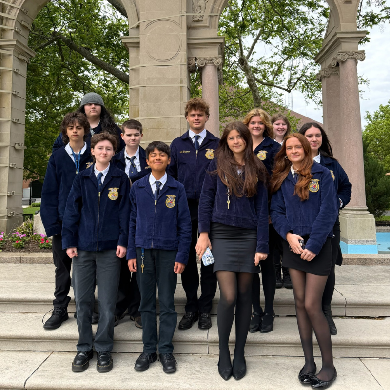 A group of young people in blue FFA jackets stand on stone steps in front of an arched structure.
