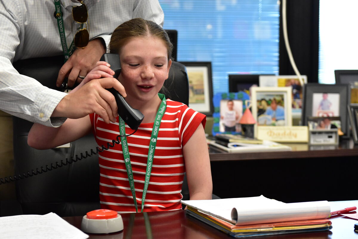 A young girl with freckles talks on a black telephone, with an adult's hand assisting.