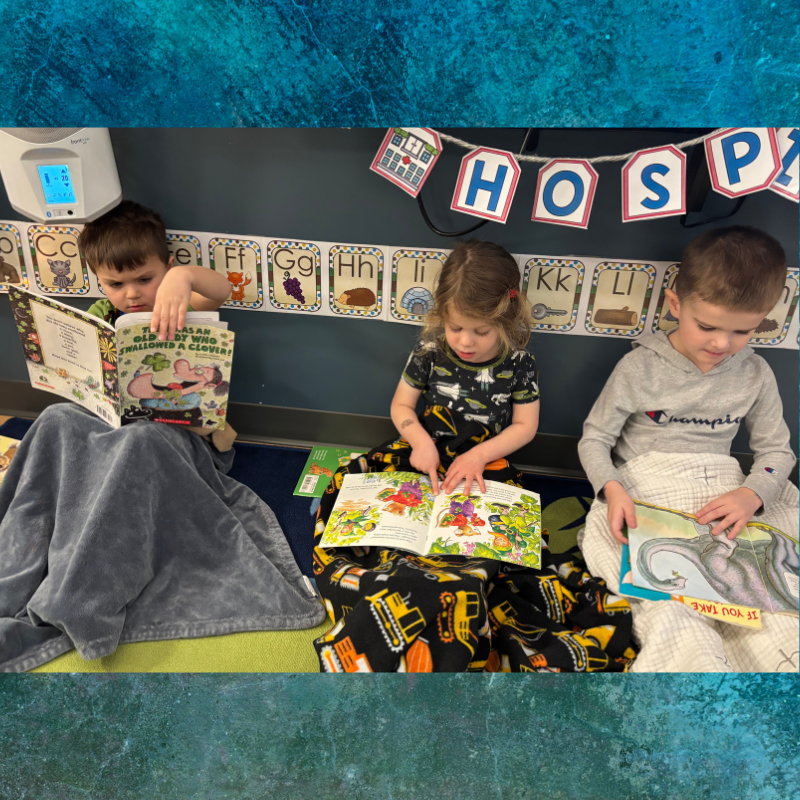 Three young children sit on the floor, engrossed in reading colorful books.