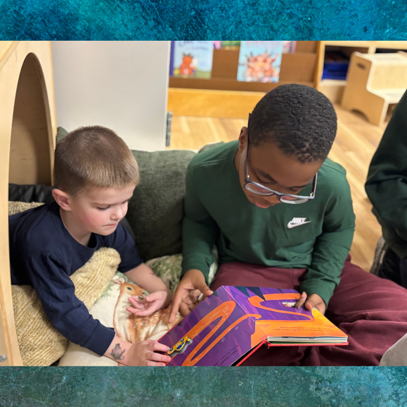 Two boys are reading a colorful book together in a cozy reading nook.
