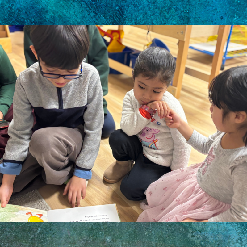 Children gather around a book, with one child pointing at the pages.