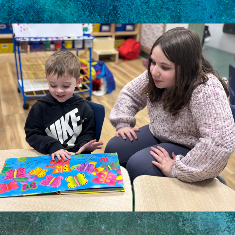Two children sit at desks and collaborate on a creative project. 