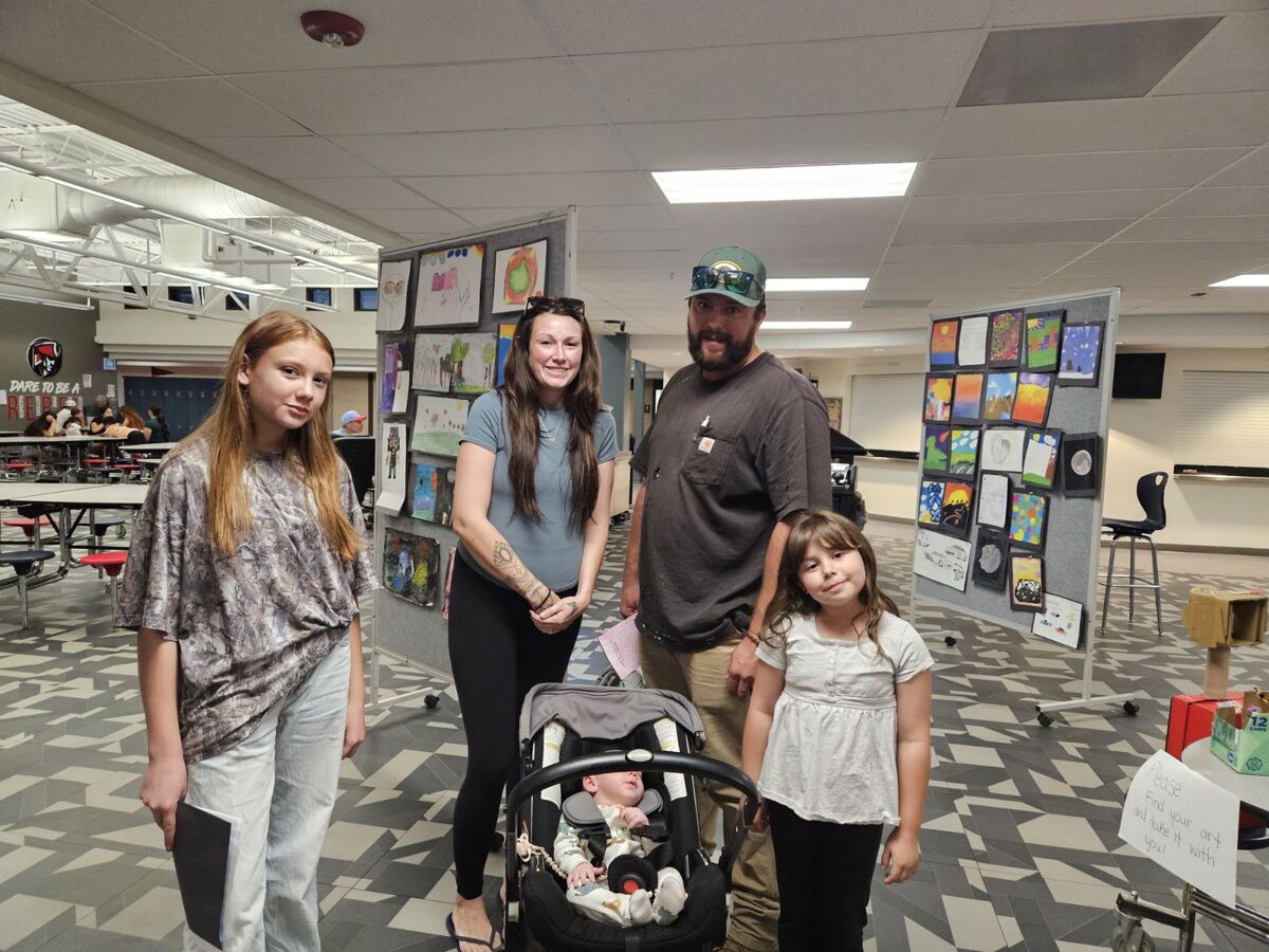 A family of five poses together inside a school hallway decorated with children's artwork displayed on boards.