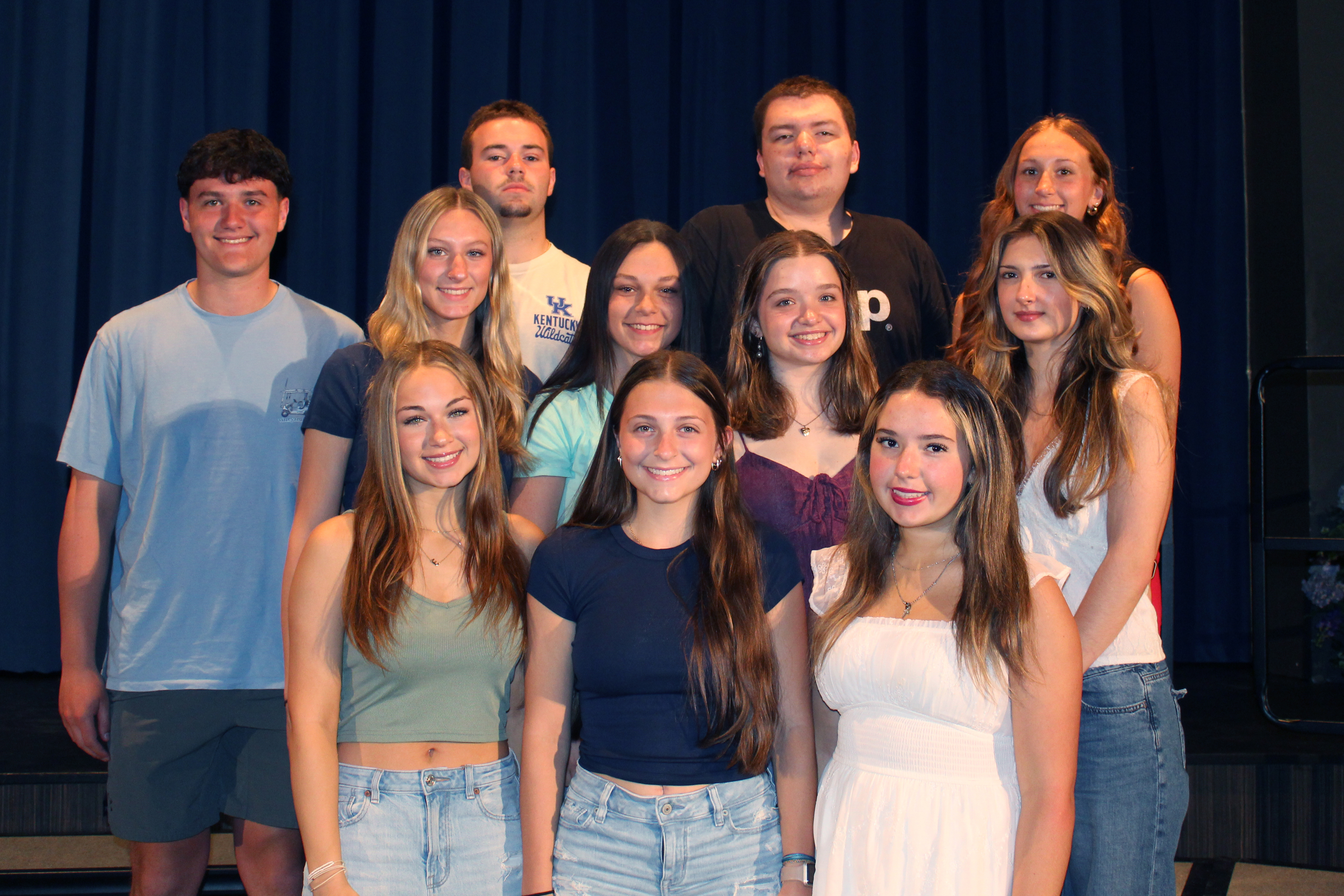 A group of young people pose for a photo in front of a blue curtain.