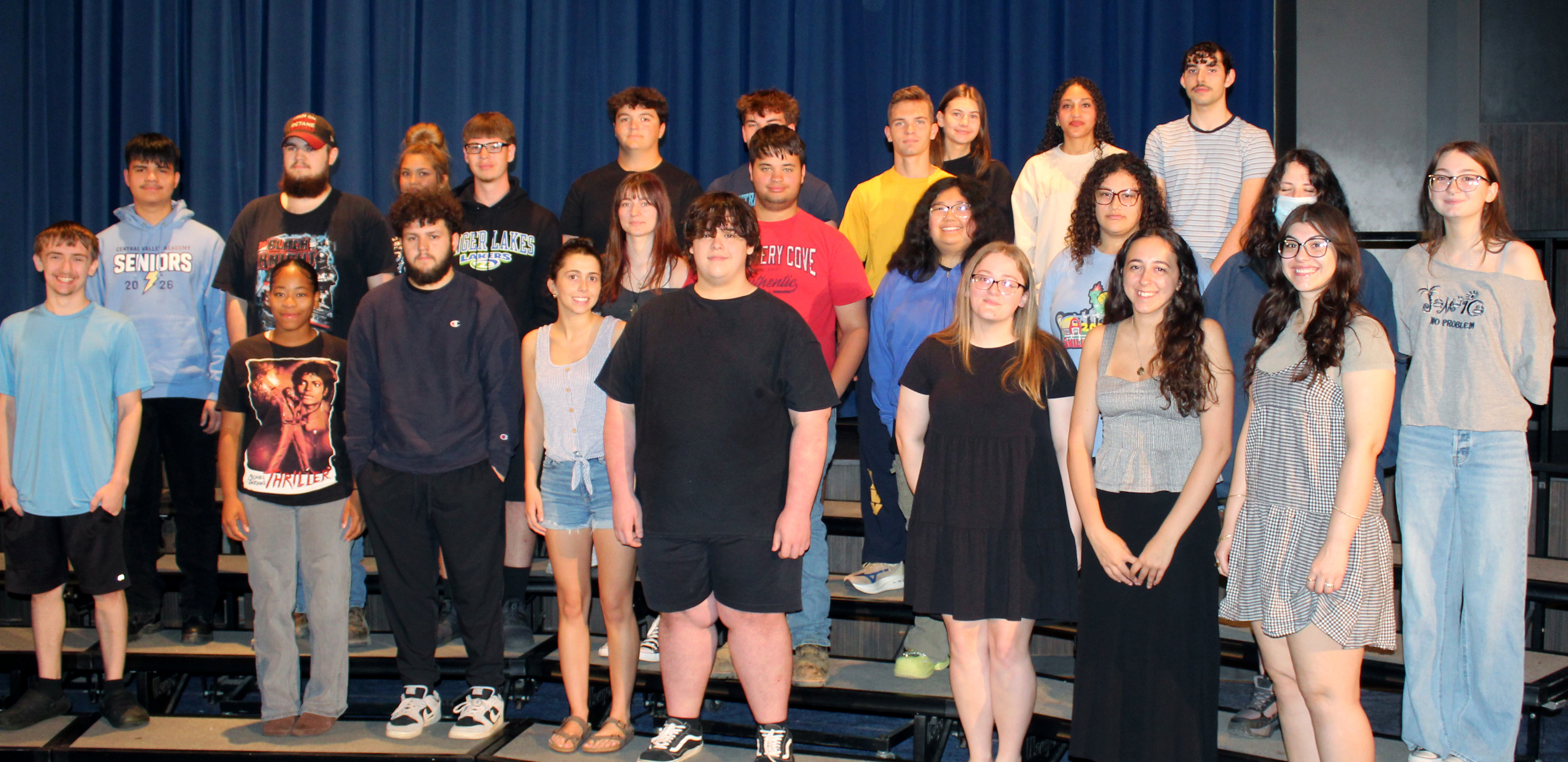 A diverse group of young adults stands on risers in front of a blue curtain.