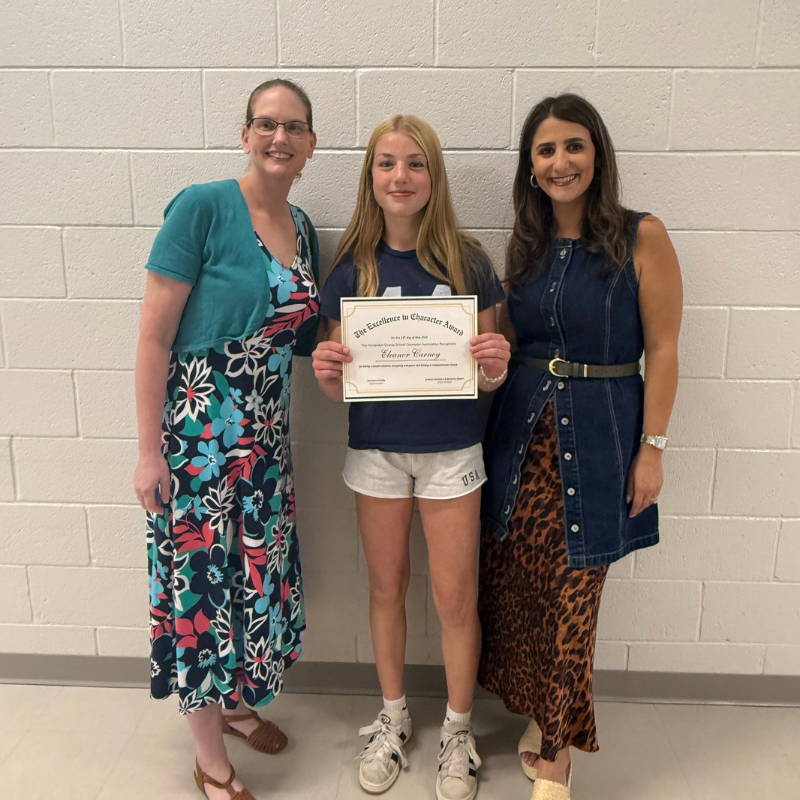 Two women stand with a young girl holding an 'Excellence in Character Award' certificate.