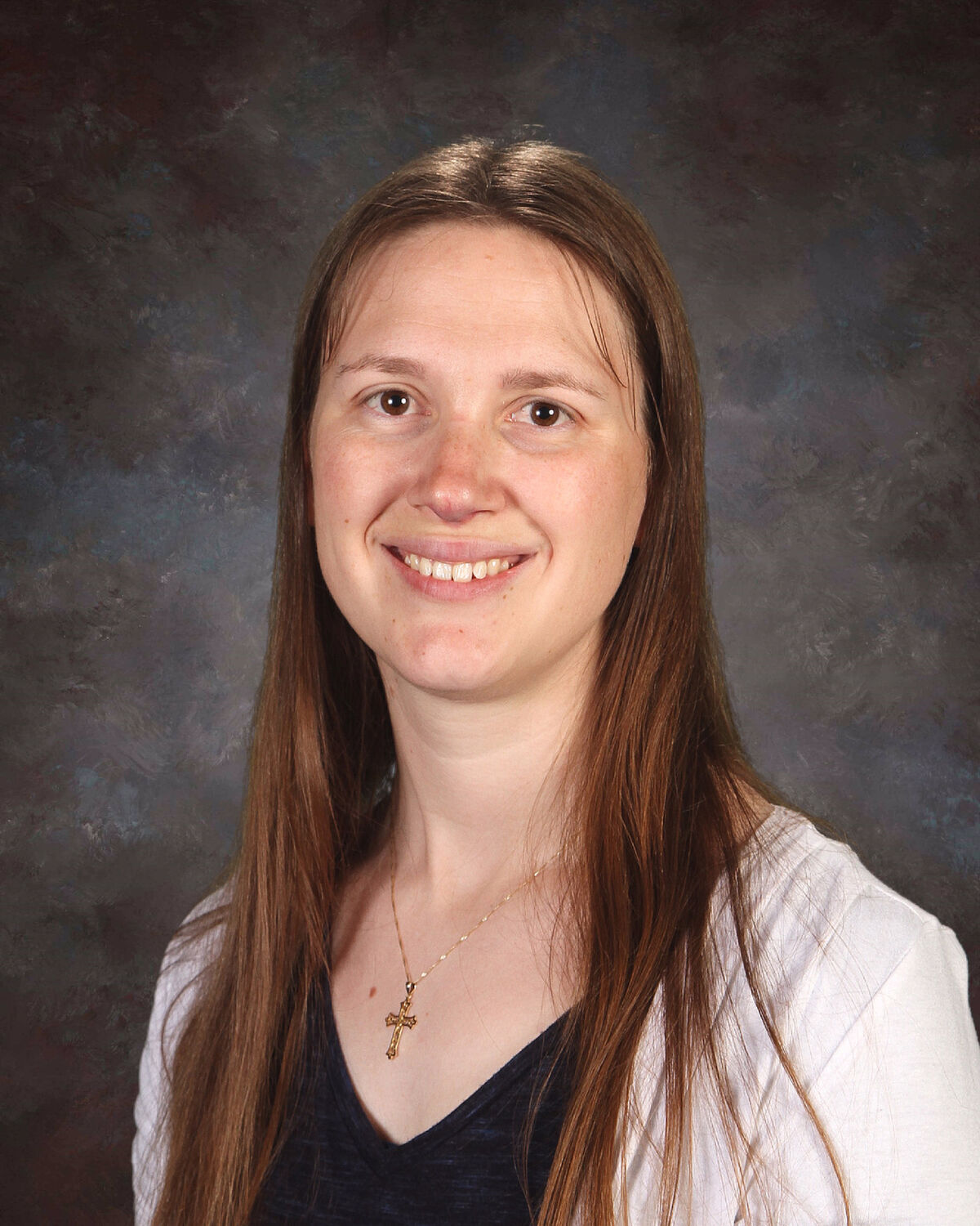 Mrs Covert,  A smiling woman with long brown hair poses in front of a dark, mottled background.