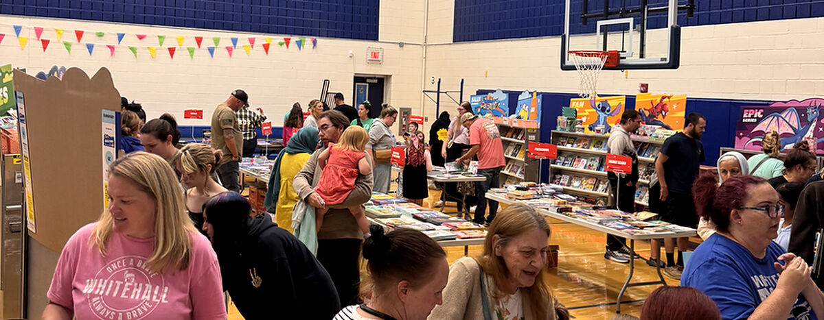 A bustling book fair inside a gymnasium, featuring tables overflowing with books and colorful displays.