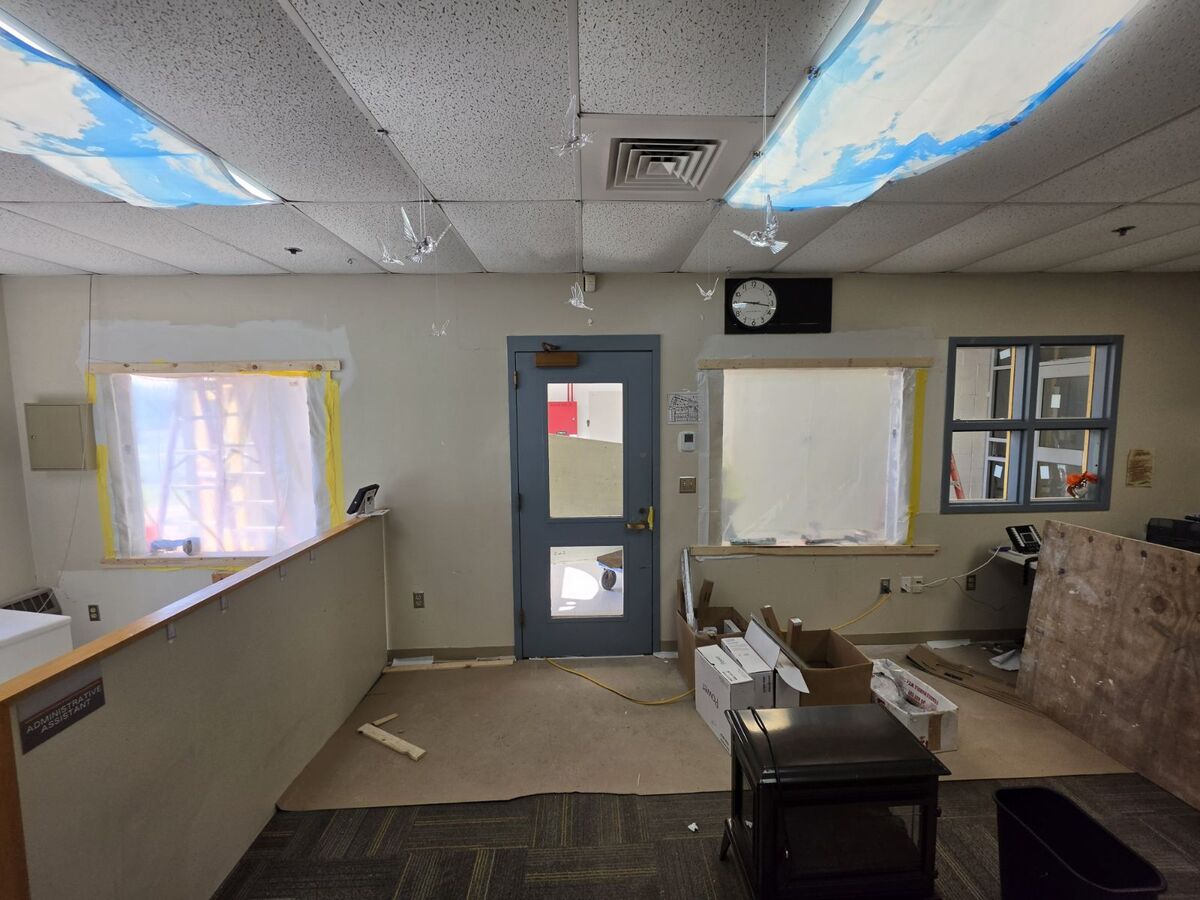 An office space undergoing renovation, with windows covered in plastic and boxes of supplies.