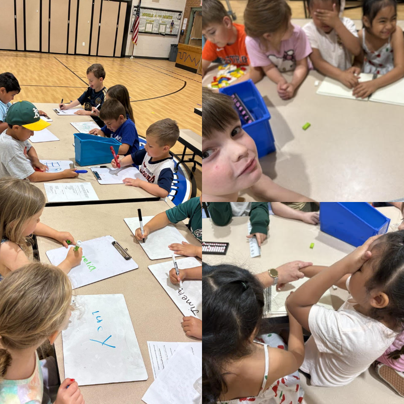 Children are seated at tables, writing on whiteboards and clipboards in a classroom setting.