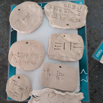 Several handmade clay tablets with cuneiform-style impressions rest on a blue-bordered cutting mat.