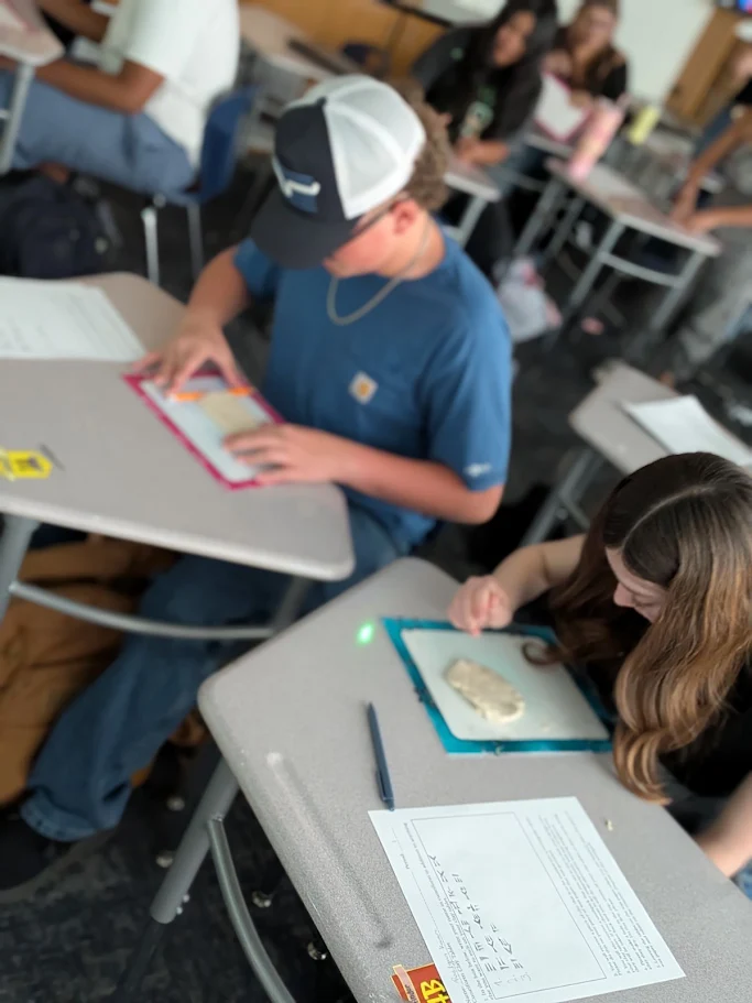 Students sit at individual desks in a classroom, engaged in a hands-on activity.