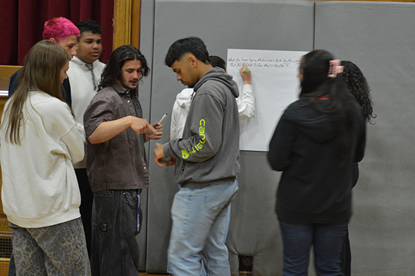 A group of young people collaborate around a whiteboard, discussing ideas.