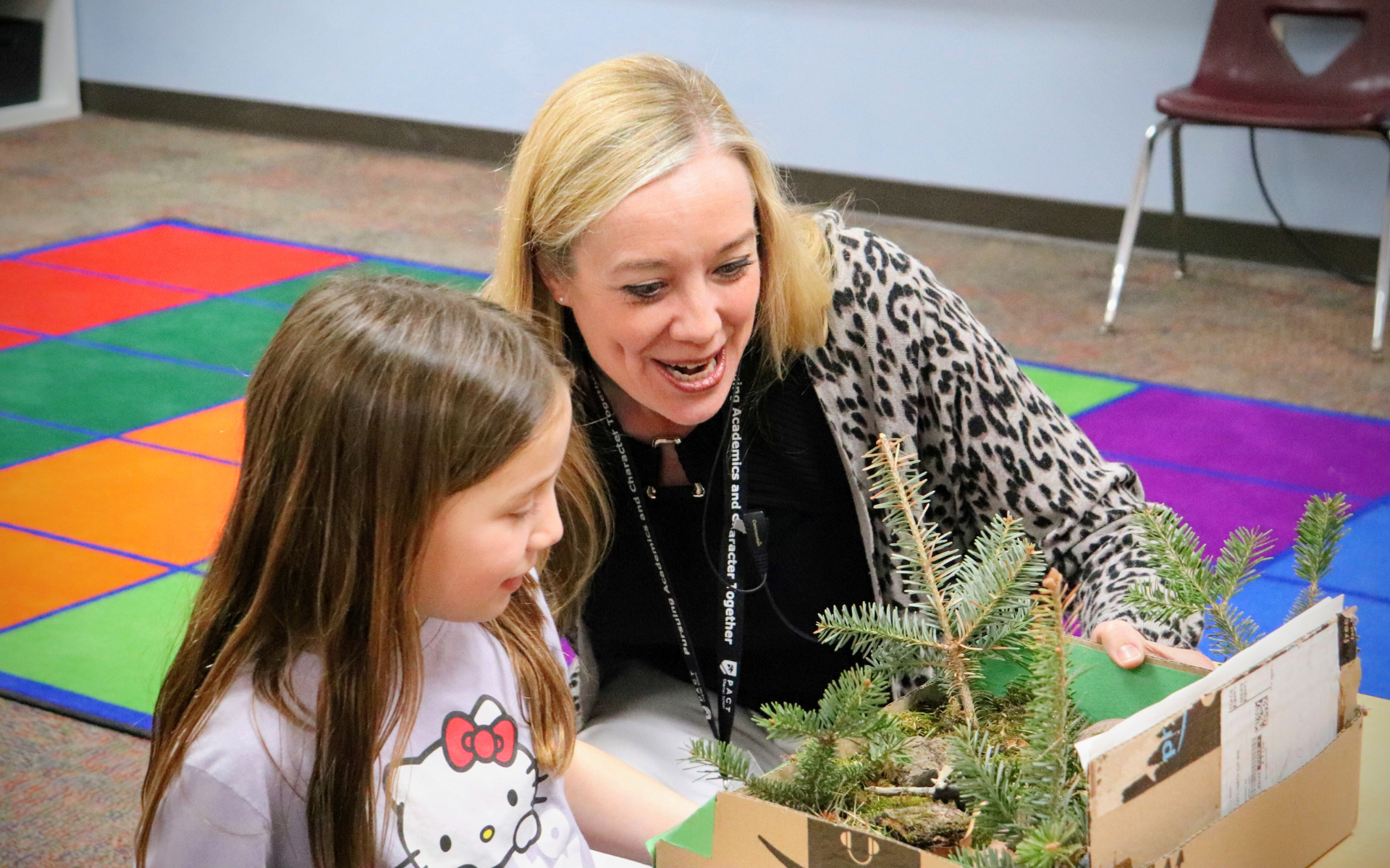 A teacher and a young student examine a miniature evergreen tree project.
