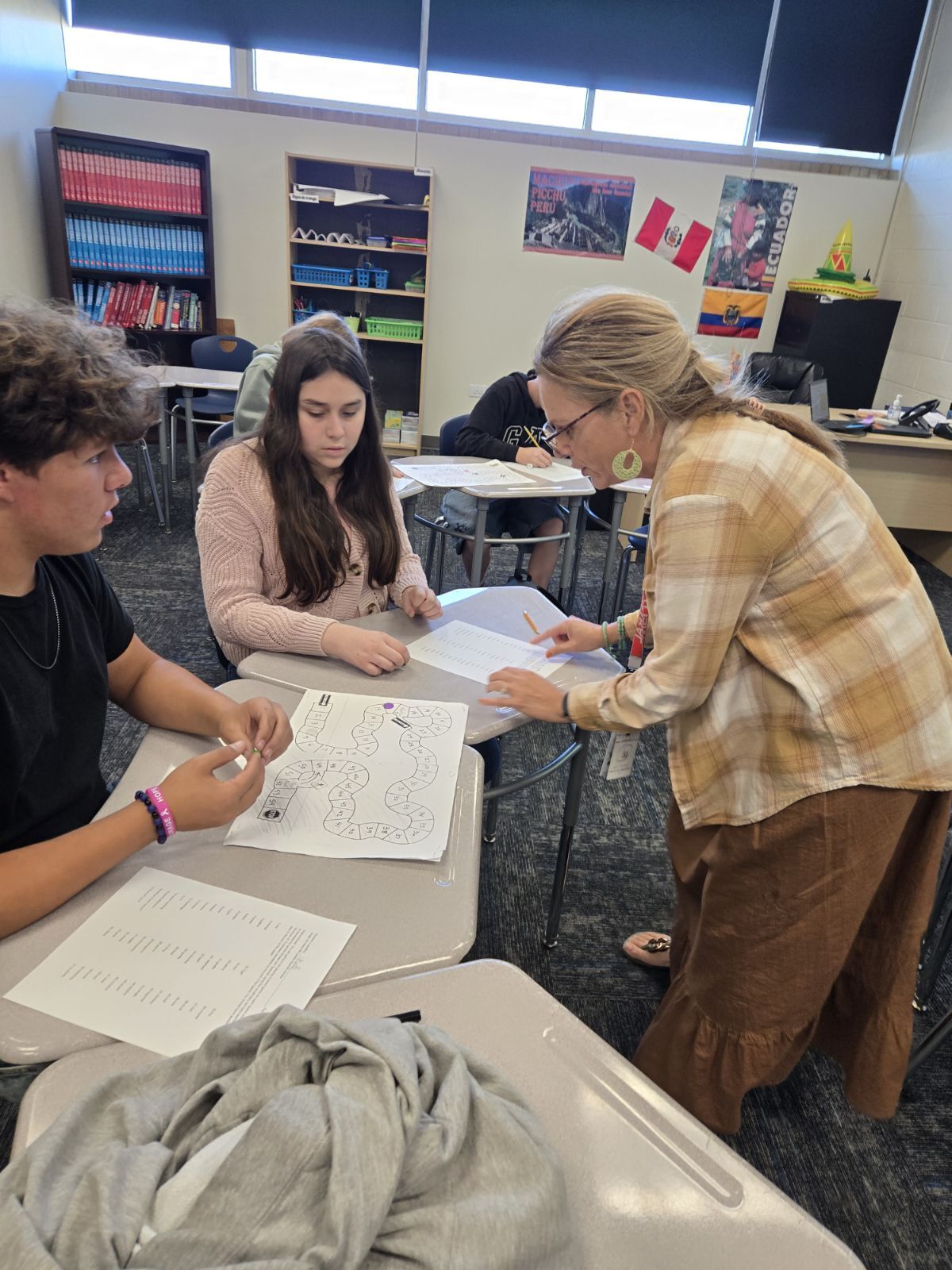 A teacher assists 8th grade students with a worksheet at their desks in a spanish classroom.