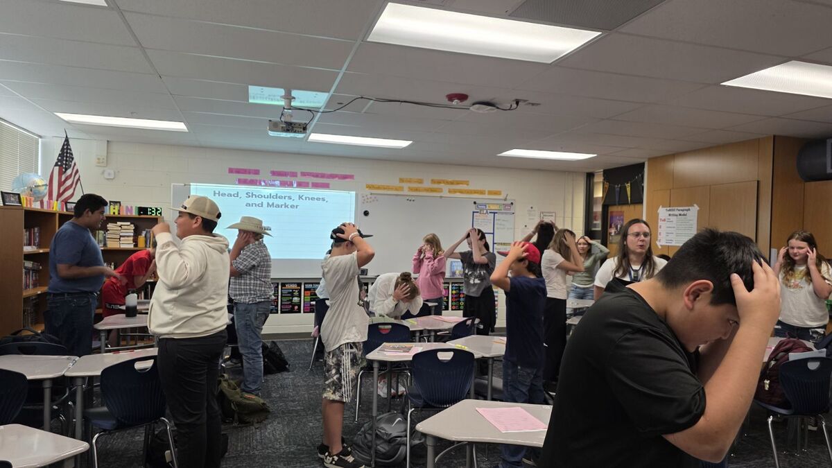 Students in a classroom are playing a game, touching their heads and shoulders.