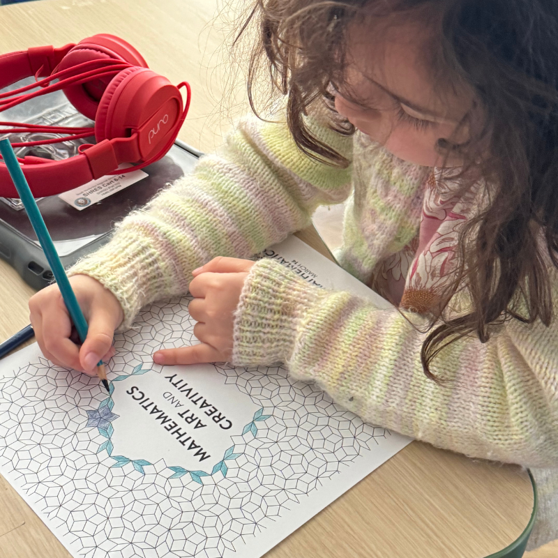 A young child with curly brown hair colors a worksheet titled 'Mathematics Art and Creativity'.