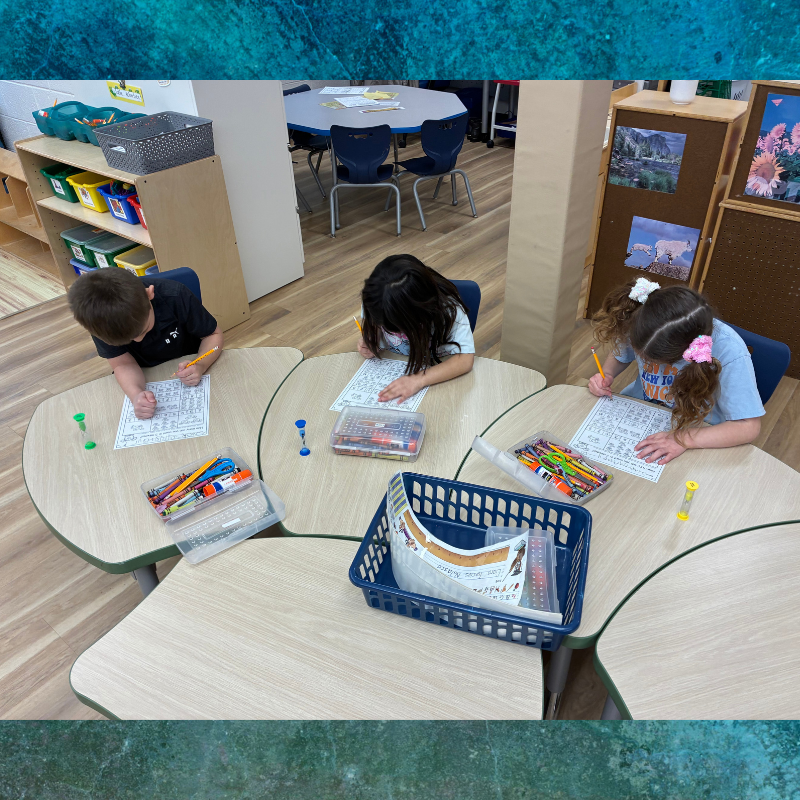 Three children focus on worksheets at individual desks in a classroom.