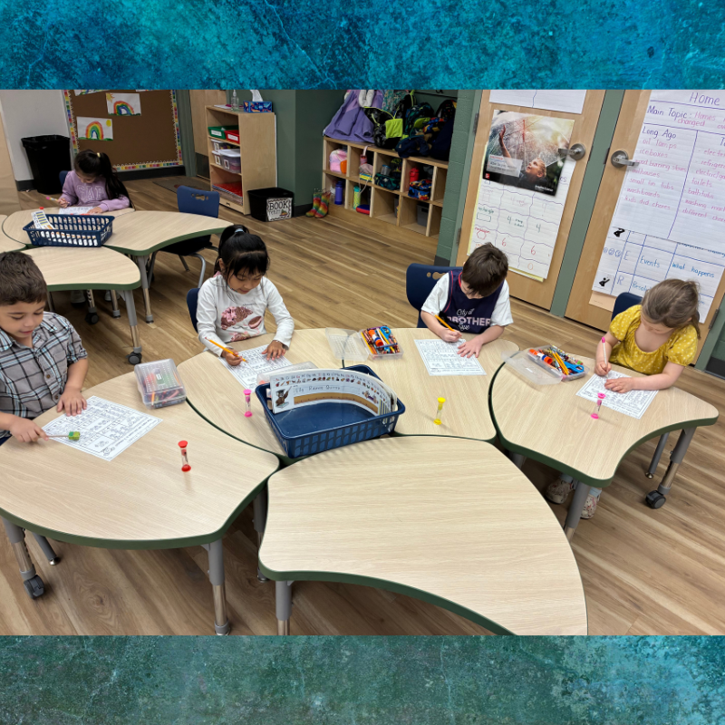 Children focus on drawing and writing at clover-shaped tables in a classroom.