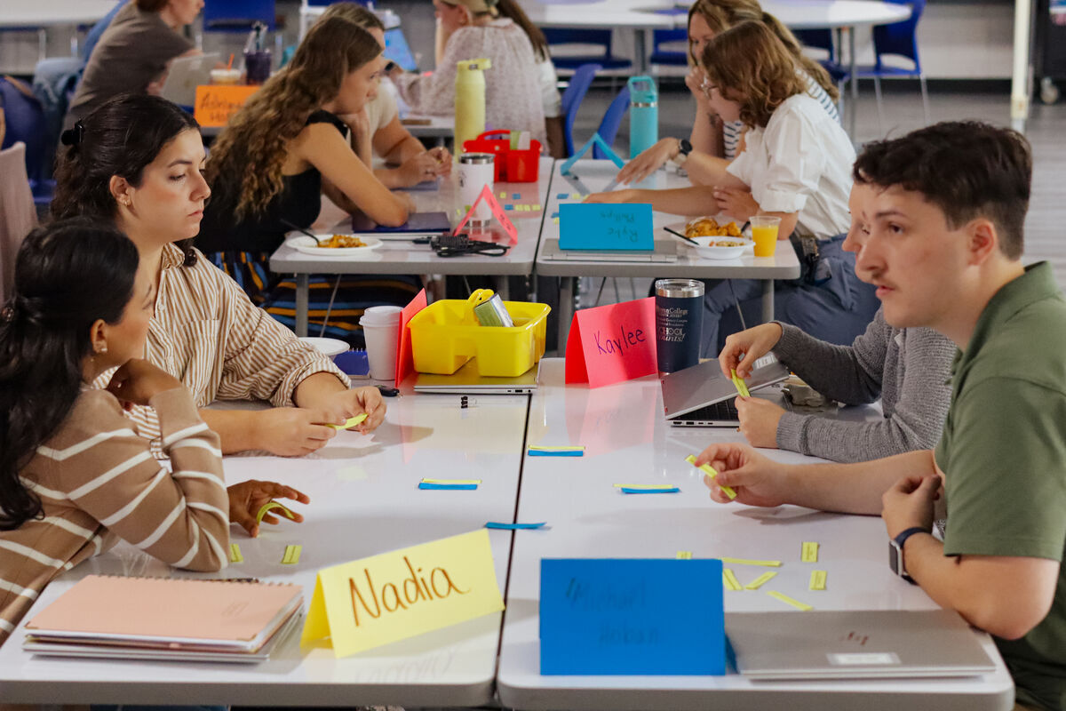 Students sit at tables, engaged in an activity with name cards and colorful materials.
