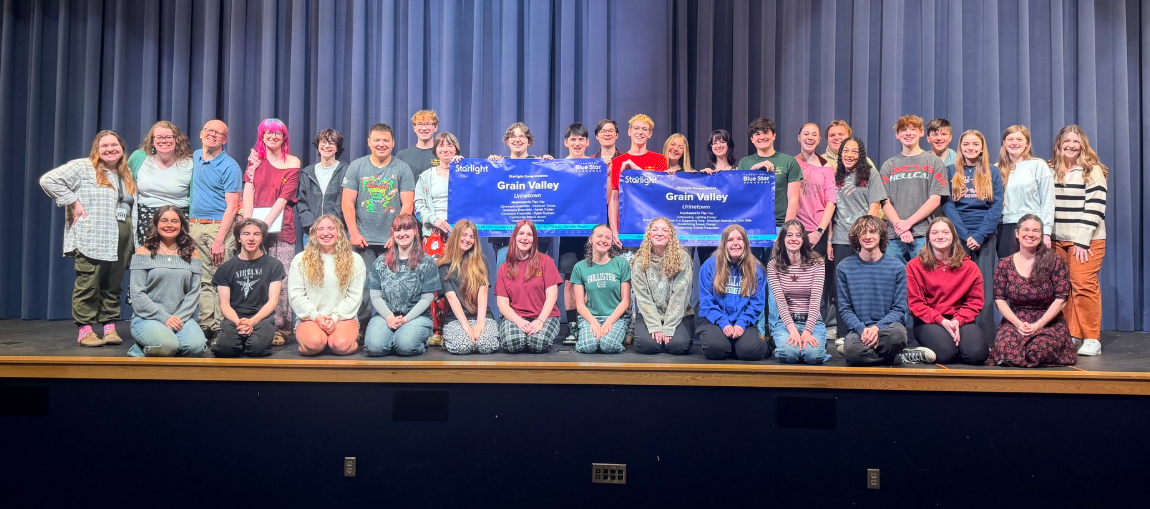 The cast and crew stand on the GVHS auditorium stage holding banners to accompany the nine blue star nominations received. 