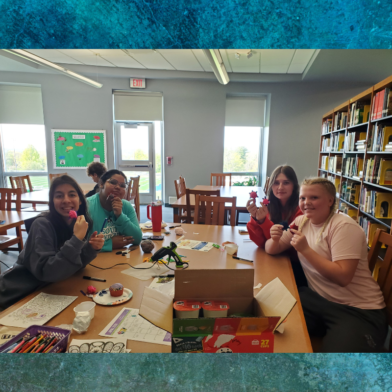 Four young people are gathered around a table, engaged in a craft activity with colorful materials.