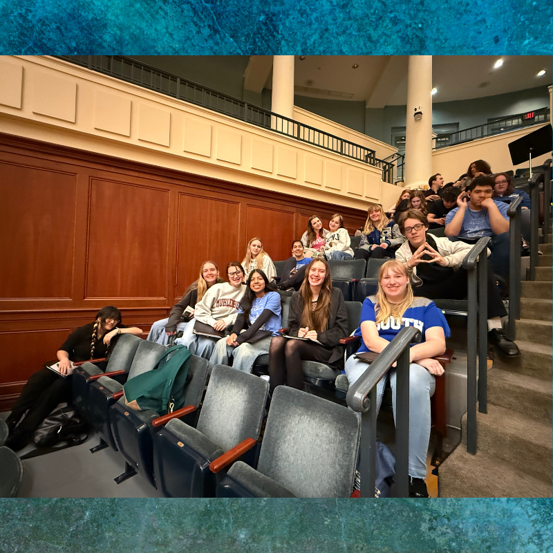 A group of young people are seated in an auditorium, smiling and looking towards the camera.