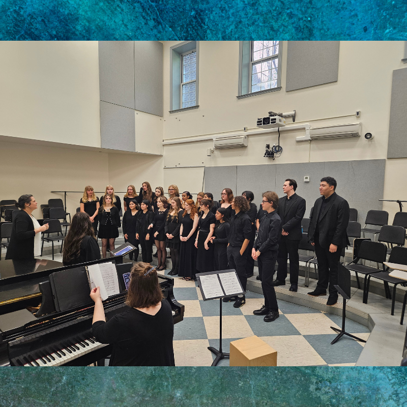A choir director leads a group of singers in a rehearsal room with a piano.