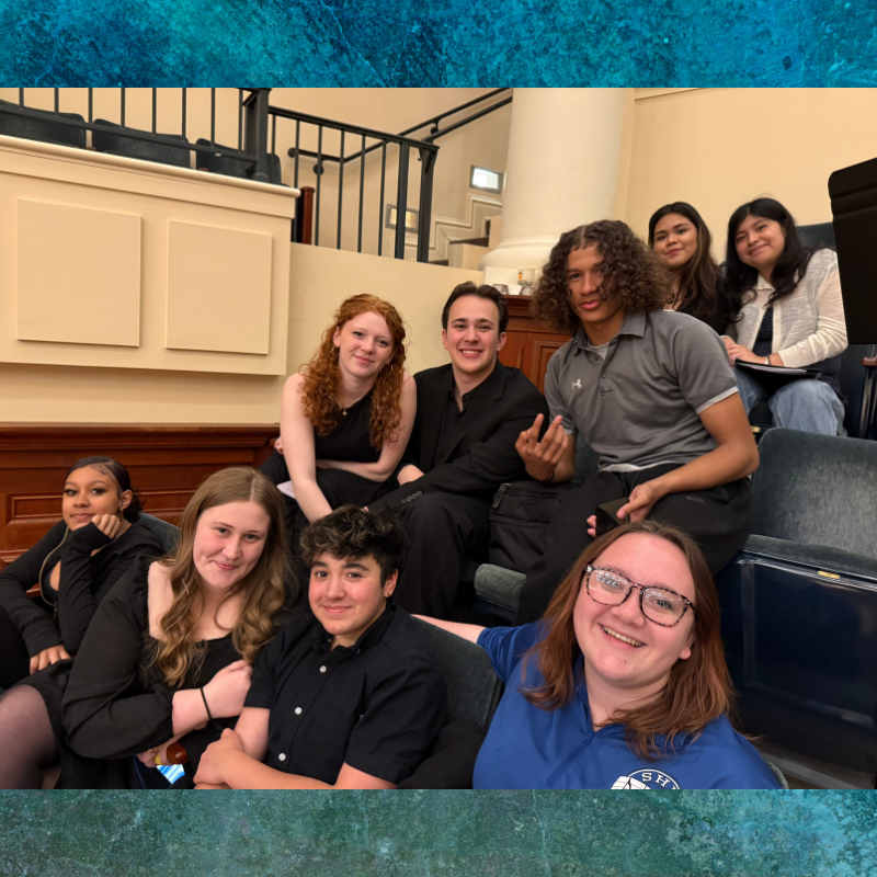 A group of young people are seated together in an indoor setting with tiered seating.