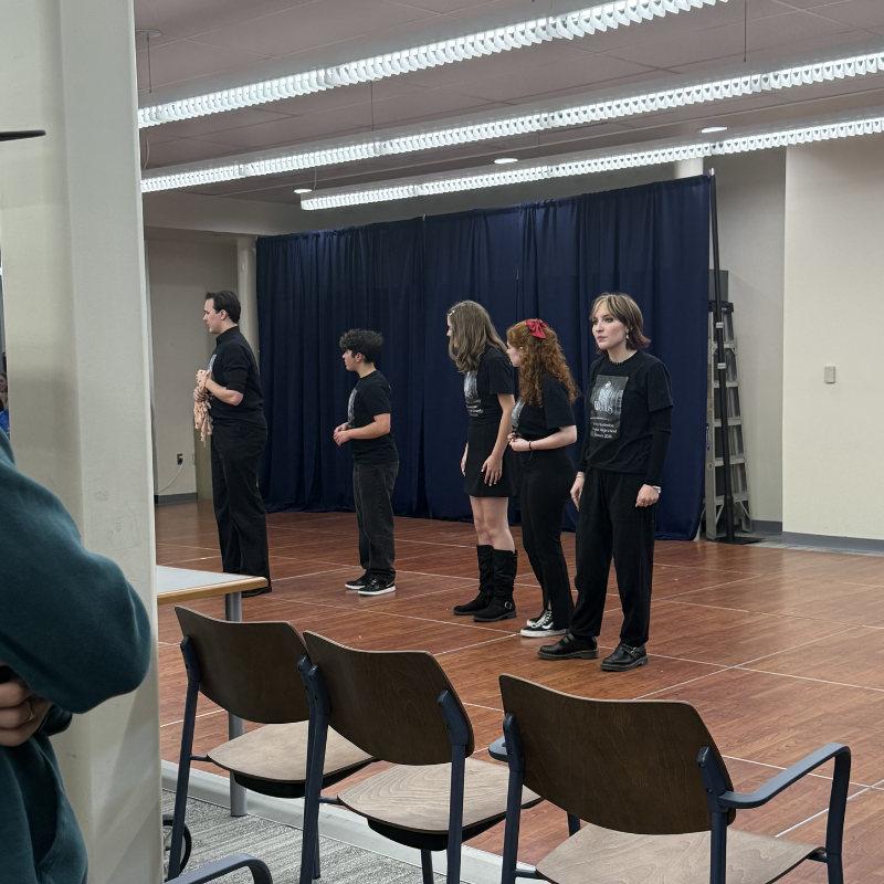 A group of young people in matching black t-shirts stand on a wooden stage.