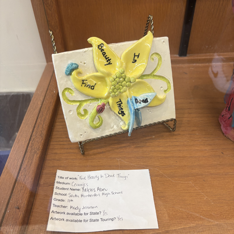 A ceramic artwork titled 'Find Beauty In Dead Things' features a yellow flower with words 'Find Beauty In Dead Things' written on its petals.