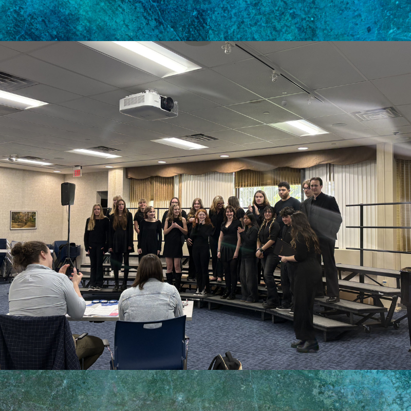 A choir of young people in black attire stands on risers, ready to perform.
