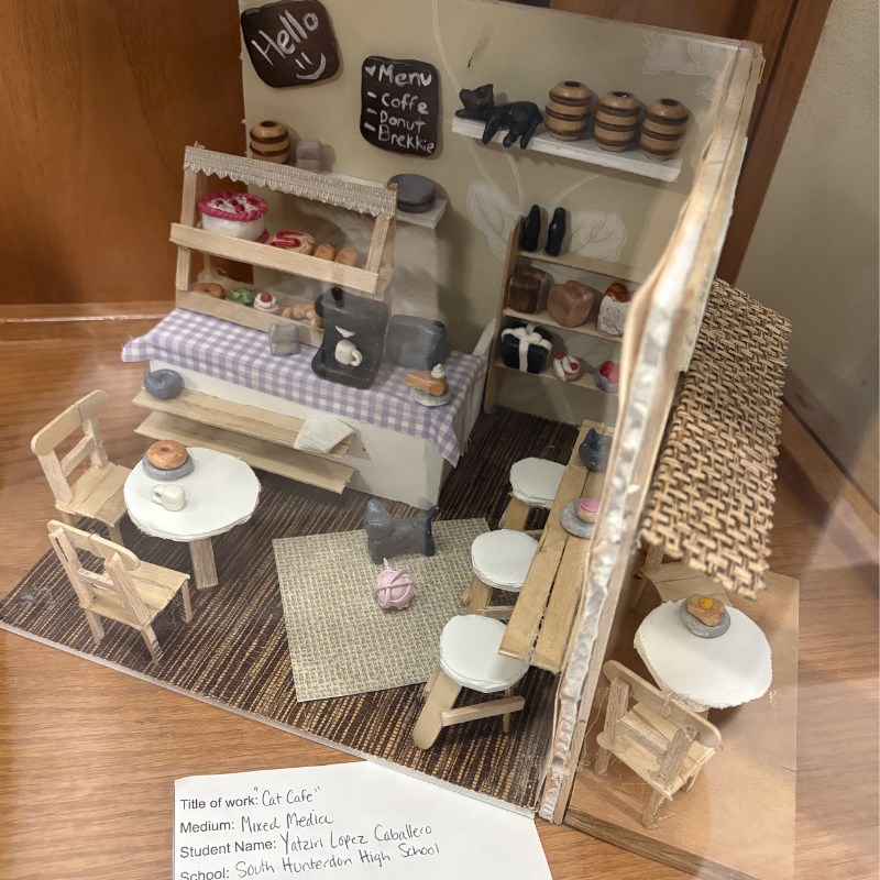 A miniature diorama of a cat-themed cafe, complete with tiny tables, chairs, and a display of baked goods.