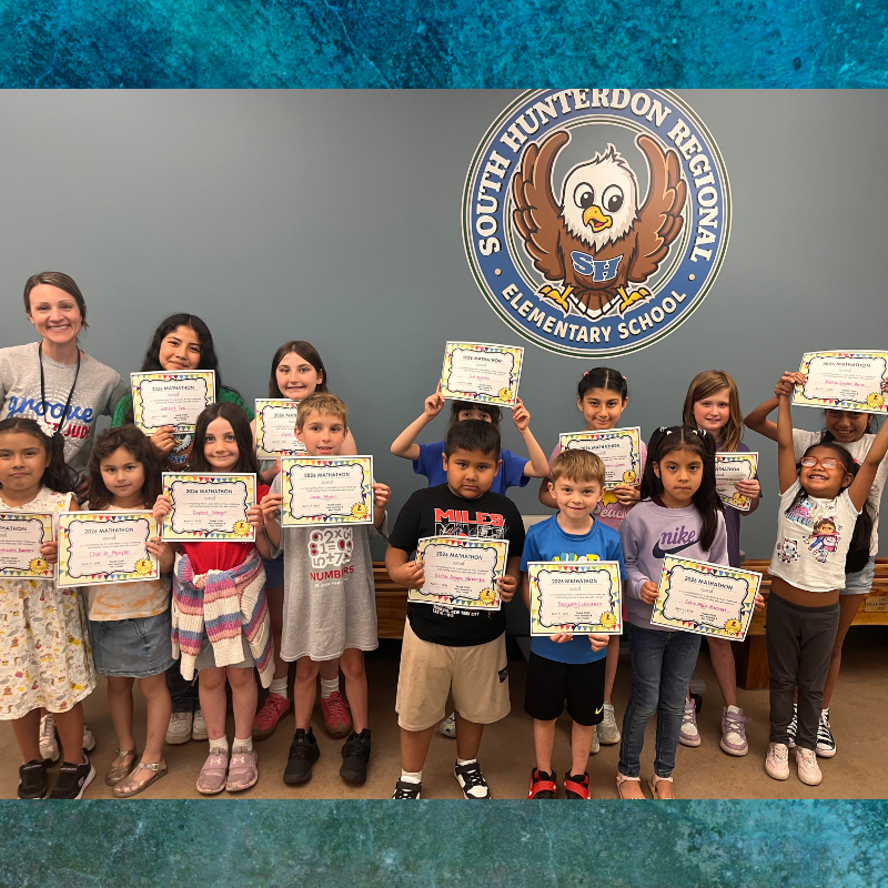 A group of smiling elementary school students proudly hold up their Mathathon certificates.
