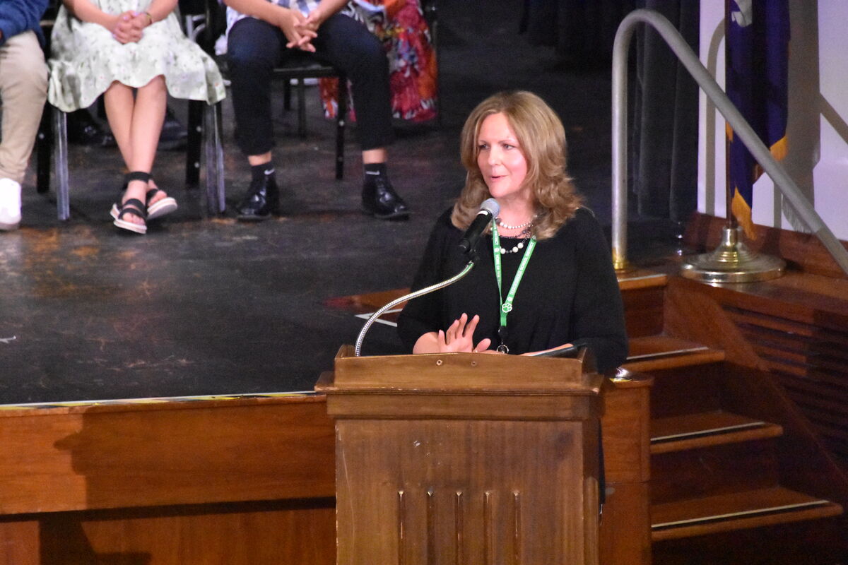 A woman speaks at a wooden podium with a microphone in front of her.