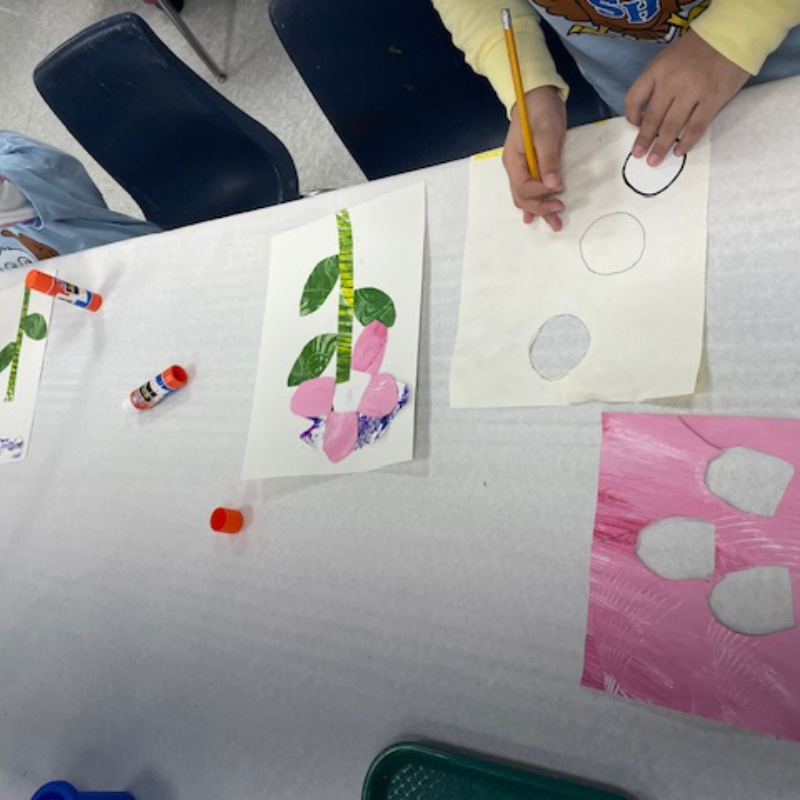 A child's hands are shown drawing circles on paper with a pencil, surrounded by art supplies.