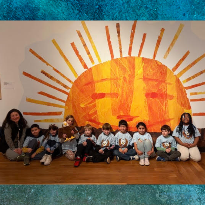 A group of children and an adult pose in front of a large, colorful sun mural.