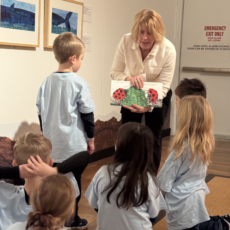 A woman reads a book about ladybugs to a group of young children in a museum.